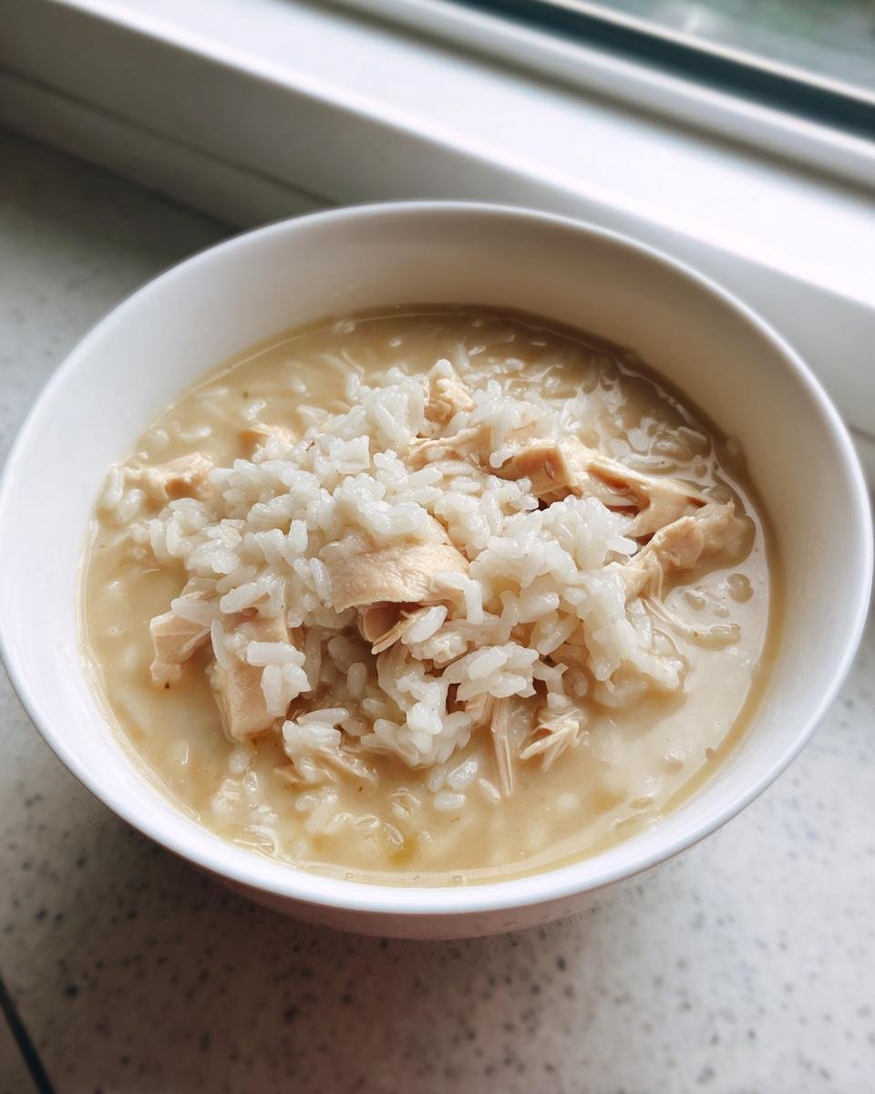 A close-up of a white bowl filled with Creamy White Chicken Rice Soup, topped generously with white rice and shredded chicken.