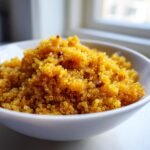 Close-up of bright yellow Curried Fried Quinoa piled high in a white serving bowl.