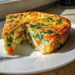 A thick slice cut from a Delicious Crustless Vegetable Quiche, showing spinach and carrots inside.
