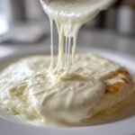Close-up of thick, creamy Easy Garlic Parmesan Sauce being drizzled from a spoon, showing excellent cheese pull over a dish.