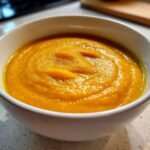 Close-up of a bowl filled with thick, vibrant orange Fall Detox Sweet Potato Veggie Soup.
