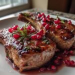 Two glazed Fancy Pomegranate Lamb Chops garnished with fresh rosemary and bright red pomegranate seeds.