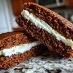 Two halves of a Gingerbread Whoopie Pie with thick vanilla buttercream filling, resting on a granite counter.