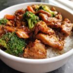 Close-up of a bowl featuring savory Chicken Stir Fry with broccoli and carrots over fluffy white rice.
