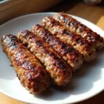Five perfectly grilled Macedonian Kebapi sausages lined up on a clean white plate, showing charred grill marks.