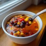 A spoonful of rich, tomato-based Hearty Vegan Taco Soup, showing black beans, corn, and diced tomatoes.
