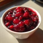 Close-up of chunky, homemade cranberry sauce recipe glistening in a small white bowl.