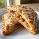 Two halves of flaky Homemade Vegan Apple Cinnamon Pop Tarts filled with spiced apples and drizzled with white icing.