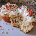 Close-up of a Homemade Vegan Funfetti Sprinkles Cupcakes cut in half, showing the colorful sprinkles inside the cake and white frosting.
