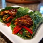 Two Honey Garlic Chicken Vegetable Rollups wrapped in lettuce leaves, filled with colorful vegetables and glistening sauce.