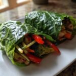 Two Honey Garlic Chicken Vegetable Rollups wrapped in large green leaves, showing filling of chicken, red pepper, and broccoli.