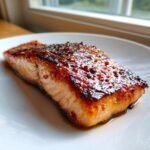 Close-up of a perfectly cooked salmon fillet coated in shiny Honey Garlic Sauce, resting on a white plate.