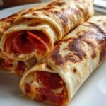 Three golden-brown Hummus Pepperoni Pizza Wraps stacked on a white plate, showing melted cheese and pepperoni inside.
