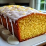 A moist, yellow Iced Lemon Loaf Pound Cake with thick white glaze dripping down the sides and lemon zest topping.