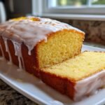 A moist Iced Lemon Loaf Pound Cake, partially sliced, featuring a thick white lemon glaze dripping down the sides.