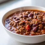 A steaming white bowl filled with rich, hearty Irresistible Easy Slow Cooker Chili featuring ground beef and kidney beans.