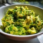 A close-up of a white bowl filled with Irresistible Herby Avocado Egg Salad, topped with fresh dill and chives.