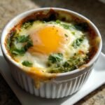A close-up of Irresistible Salsa Verde Baked Eggs cooked in a white ramekin with melted cheese and fresh cilantro.