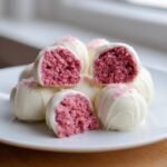 Close-up of Irresistible Strawberry Cheesecake Truffle Balls coated in white chocolate, showing the pink, crumbly interior.