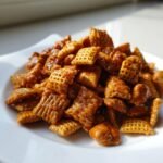 A close-up pile of crispy waffle cereal squares coated in shiny, golden-brown toffee glaze for the Irresistible Toffee Chex Mix recipe.
