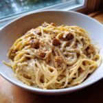 Close-up of a bowl of Irresistible Vegan Carbonara with creamy sauce and seasoned vegan bacon bits.