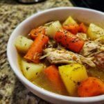 Close-up of shredded chicken, large carrot chunks, and potato pieces in the broth of Jamaican Chicken Soup.