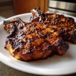Two thick, juicy pork chops covered in a dark, glossy Jerk Sauce Grilled Pork Chops glaze on a white plate.
