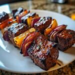 Close-up of perfectly grilled, juicy steak kabobs threaded with red onion and yellow bell pepper chunks.
