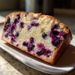 A close-up slice of moist Lemon Blueberry Cream Cheese Pound Cake with visible blueberries in a rich yellow crumb.