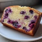 Close-up of a moist slice of Lemon Blueberry Cream Cheese Pound Cake showing rich purple blueberries baked into the yellow crumb.