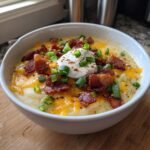 A creamy bowl of Loaded Baked Potato Soup garnished generously with cheddar cheese, bacon bits, sour cream, and green onions.