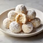 A stack of creamy Mascarpone White Chocolate Truffles dusted heavily with powdered sugar, one is broken open.