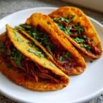 Three crispy, golden tacos filled with shredded jackfruit birria and topped with fresh cilantro.