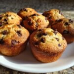 Close-up of several golden brown Mini Chocolate Chip Muffins studded with dark chocolate chips, served on a white plate.
