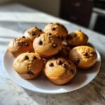 A pile of freshly baked Mini Chocolate Chip Muffins with visible chocolate chips on top, served on a white plate.