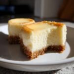 Close-up of two New York Style Cheesecake Bites on a white plate, one with a bite taken out.