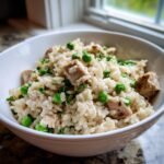 A white bowl filled with creamy One Pot Ranch Chicken Rice mixed with bright green peas and herbs.
