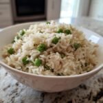 A white bowl filled with fluffy One Pot Ranch Chicken Rice mixed with bright green peas, resting on a granite countertop.