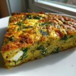 A thick slice of Orzo Frittata With Spinach And Feta showing cooked orzo pasta, green spinach, and white feta cheese pockets.