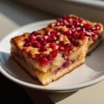 Two slices of Pomegranate Apple Pie Bars with a golden crust and topped with bright red pomegranate seeds, served on a white plate.