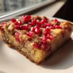 A close-up of a square slice of Pomegranate Apple Pie Bars topped with bright red pomegranate seeds.