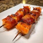 Two skewers of perfectly cooked Prosciutto Wrapped Salmon Skewers, glistening and slightly charred.