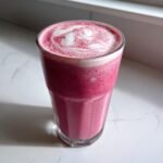 A tall glass filled with a vibrant pink Raspberry White Chocolate Smoothie, topped with a white swirl.