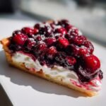 A close-up slice of a Roasted Berries Tart featuring a buttery crust, thick cream filling, and glossy roasted berries topped with powdered sugar.