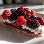 Close-up of a slice of Roasted Berries Tart topped with fresh raspberries, blackberries, and whipped cream.