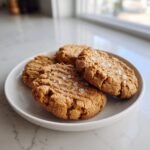 Four delicious Salted Peanut Butter Cookies Gluten Free, sprinkled with flaky sea salt, resting on a white plate.