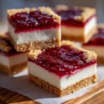 Close-up of stacked Shortbread Raspberry Cheesecake Bars showing a thick shortbread crust, creamy white filling, and bright raspberry topping.