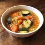 Close-up of a white bowl filled with Slow Cooker Quinoa Veggie Soup featuring carrots and zucchini.