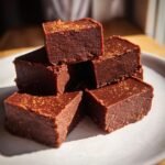 A stack of rich, dark brown Spicy Mexican Hot Chocolate Fudge squares dusted with spice on a light plate.