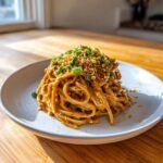 A serving of Spicy Peanut Noodles coated in sauce, topped with chopped peanuts and green onions.